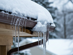 Close-up of a residential gutter system burdened by heavy snow and hanging icicles during a Maryland winter storm, showing potential ice damming and structural strain.