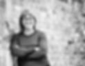 black and white Image of a female smiling with glasses on, leaning against a brick wall