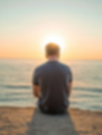 Ein junger Mann sitzt zusammengesunken am Strand und blickt auf das Meer