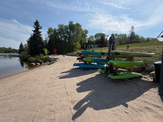 Kayaks and paddleboards on a rack by a sandy beach.