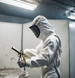 a man in a white paint suit spray painting a metal object in a spraying booth.jpg