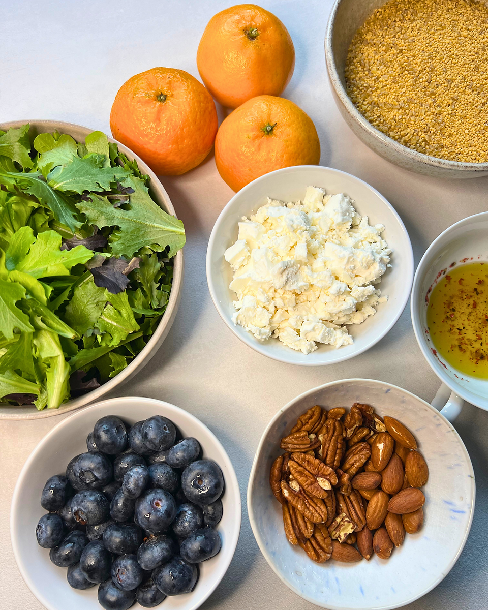 Winterliche High-Protein Salat Bowl mit Clementinen und Rote-Linsen-Couscous, Salat, weißer Tisch, Blaubeeren, Holzlöffel, Pekannüsse, Mandeln, Olivenöl, Leinöl