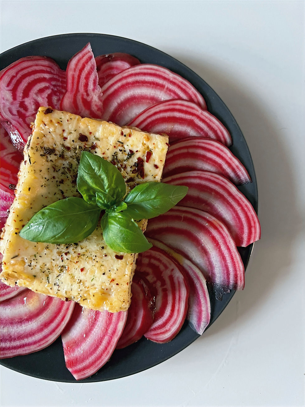 Ringelbete Carpaccio auf schwarzem Teller mit gebratenem Feta, Basilikum und Gewürzen auf weißem Hintergrund.
