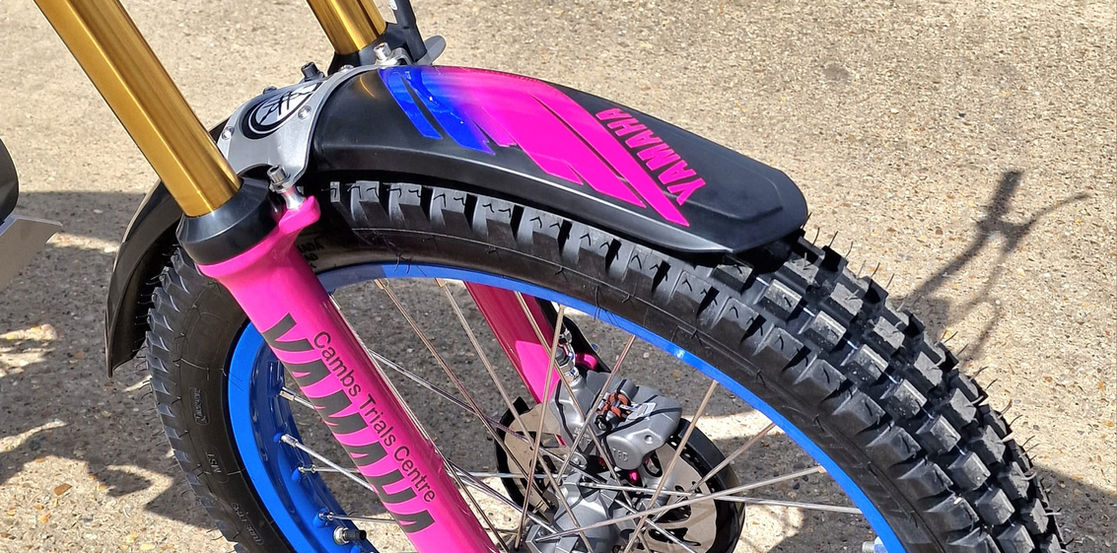 Close-up of a Scarpa trial bike front wheel with blue rim and pink accents.