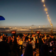 Rooftop sunset crowd: Crowd of professionals at a rooftop networking event at sunset with string lights overlooking San Diego