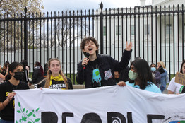 Gabrielle energetically speaks into a microphone at the Fridays for Future rally, with the White House in the background. In front of Gabrielle is a banner, held up by rally organizers.