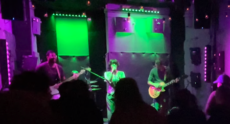 Friends and Amigos perform onstage under green and purple lights at The Pocket DC