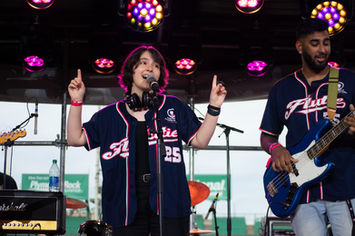 Performing onstage at Fenway Park, Gabrielle holds up a finger on each hand, signaling to the crowd that they are on round 1/4 of the "Sitting on Tables" sing-along section 