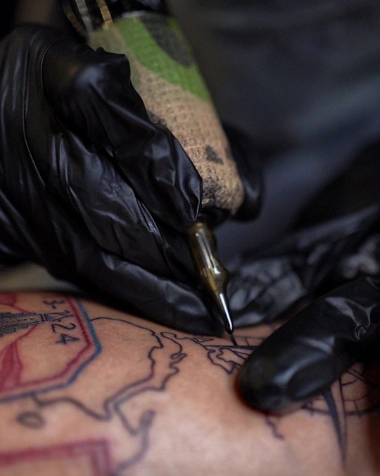 Close-up of a leg tattoo featuring a detailed map design with stamps, compass, and landmarks, done in linework and color shading.