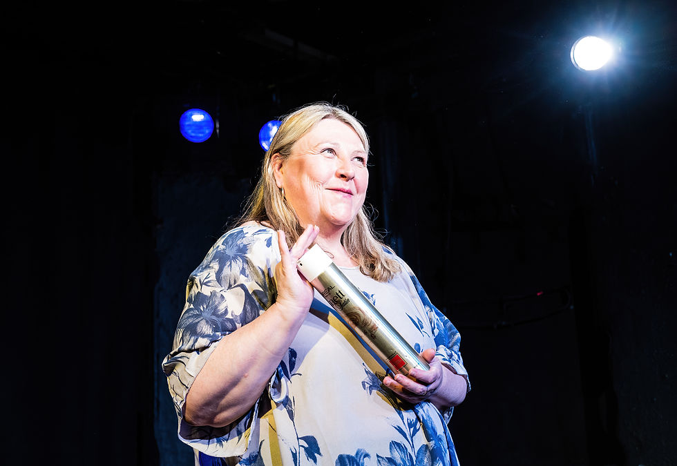 Joann Condon smiling on stage holding a can of hairspray