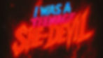 Text "I Was a Teenage She-Devil" in bold blue, pink, and fiery red fonts on a dark, smoky background, creating an intense mood.