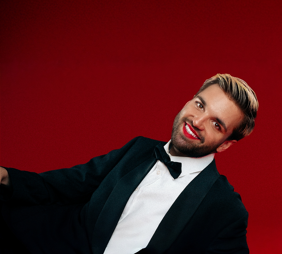 Will Owen dressed in a tuxedo with red lipstick, smiling confidently against a bold red background.
