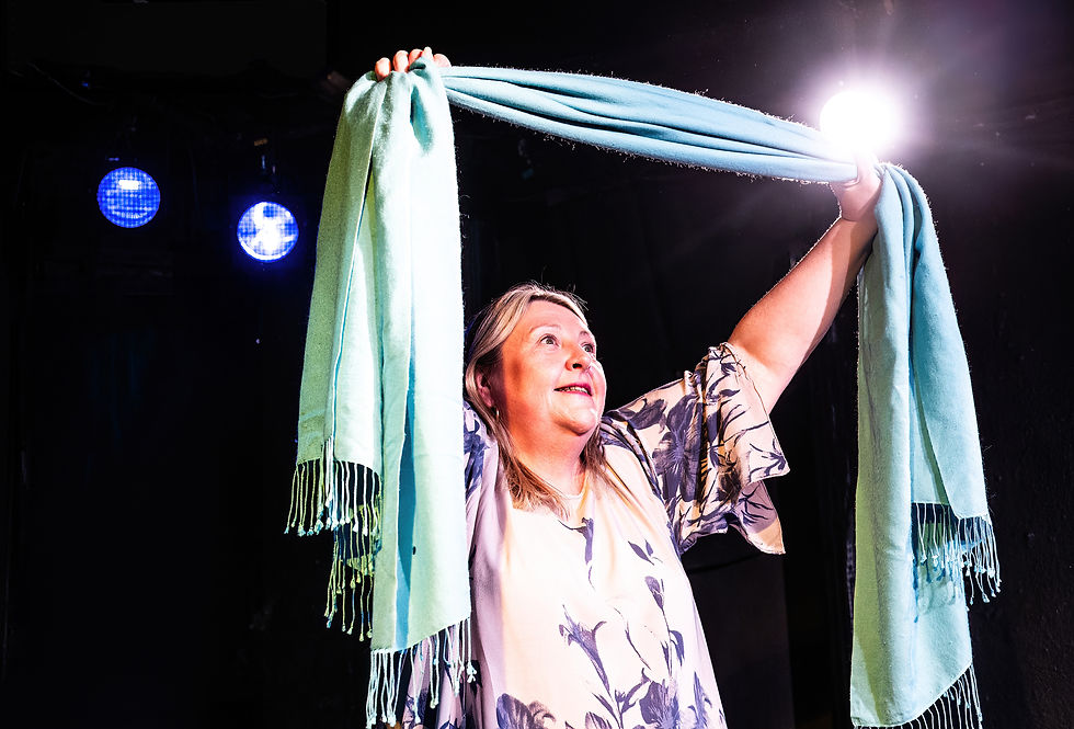 Joann Condon raising a turquoise scarf under stage lights