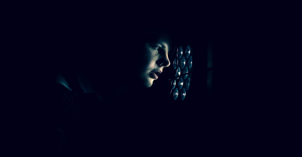 Person's face lit by a grid of circular lights in a dark setting, creating a mysterious, contemplative mood. No text present.