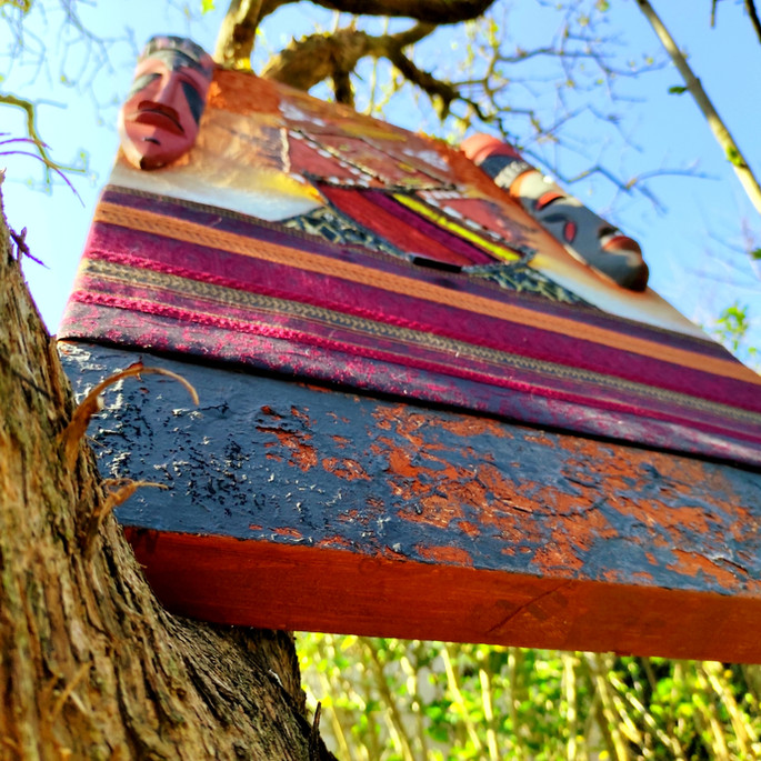 "Fomba" is a departure from Marie AVA's typical artistic style, but it's a necessary one to convey both the artist's personal journey and that of her entire collection, "Tany," which revolves around the concept of Earth and origins.

This piece explores sculpture to emphasize the omnipresence of our social masks, which often conceal our deeper truths and identities. These masks are deeply rooted in our origins, in the very soil of our upbringing – the earth of our ancestors, where we will all rest one day.

The soil represents our conditioning (specifically collected at a depth of 30 meters for its symbolism of deep roots) and the environments in which we grow. It also emphasizes the significance of the ancestral land where we will eventually rest.

The attempt to present fabric as a full-fledged relief, especially that of noble textiles, serves as a reminder that this element adorns us and tells the story of the caste, family, or social class from which we hail. Yet, in death, it will also serve to cover and accompany us into the red earth we once trod upon but will eventually be buried within.

The presence of leather symbolizes the immutability and rigidity of these conditionings, social pressures, and our occasional struggles to break free from them. Therefore, it is only partially embedded within the canvas, not completely.

Furthermore, "Fomba" denounces the obligation for gender-fluid or unknown individuals to disguise themselves and hide behind masks to survive and be accepted by their families and in such archaic societies. It carries a powerful message. The masks' similarity, without clear indications of feminine or masculine identity, challenges fundamental ideas in traditional societies and cultures that insist on a heterosexual family model. It pays tribute to Marie's deep commitment to respecting individual gender and identity over the normative rules established by our ancestors and the status quo.