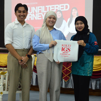 Imamull Qhaeer, Amal Osmera (left) and lecturer (right) smiling, holding a Kolej IGS totebag, something is projected behind the screen