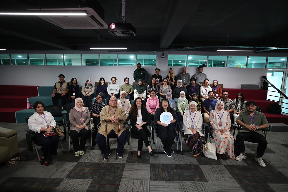 A diverse group of people pose smiling in a modern auditorium with red and teal seating. One person holds a sign with "YSEALI" text.