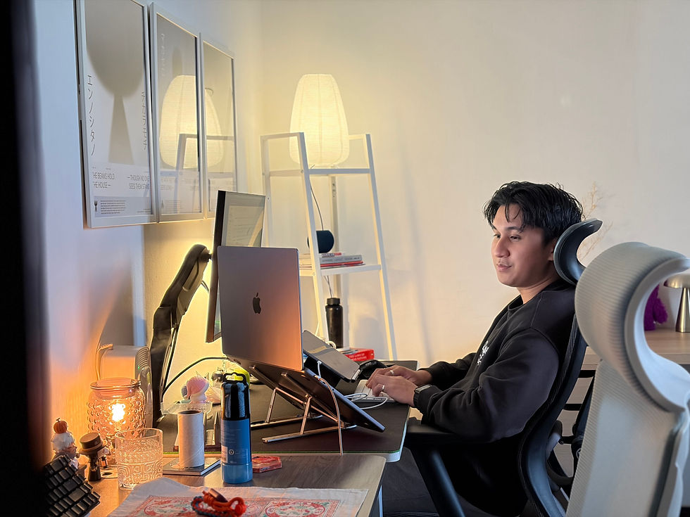 Man typing at a desk in a warm-lit home office, with an open MacBook, glowing lamp, and framed Japanese posters on the wall.