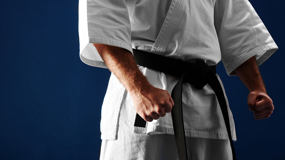 Close up of a karate student's black belt with white uniform on a black background