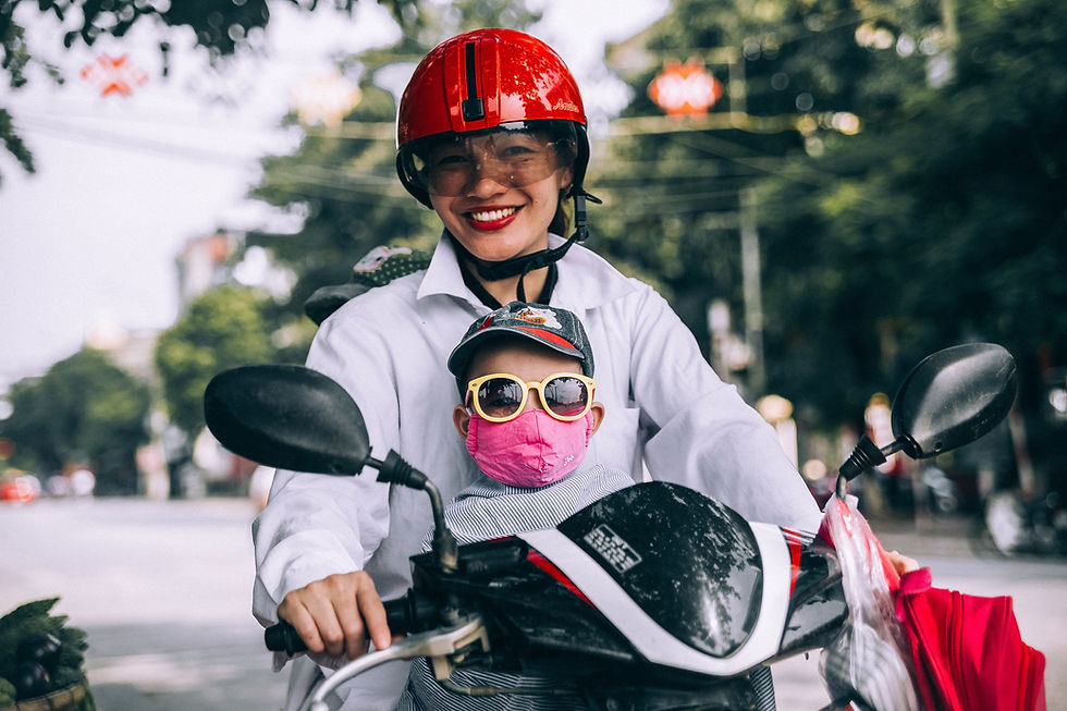 Femme portant un casque rouge sur un scooter avec un enfant devant elle.