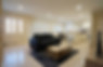 Two (2) bedroom aprtment lounge room with a sofa, coffee table, and TV, you can see the open style kitchen and dining table behind the lounge and the front door to the unit