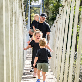 Dad and kids running joyfully along the old swing bridge in Cooranbong during a playful, candid family photography session