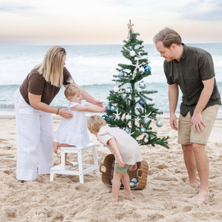A family decorate a Christmas tree together during Central Coast mini sessions at the beach