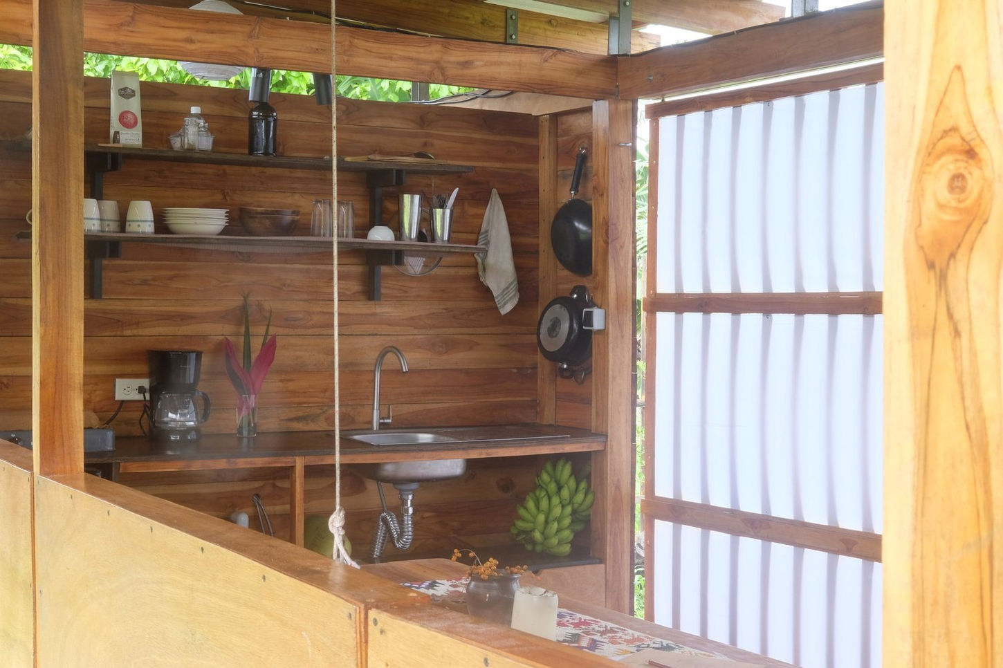 The Camper House, designed by architect Dani Serrano, is an experimental project in Nicaragua that integrates a refurbished campervan into a larger, purpose-built wooden structure. Created with a small budget and simple construction methods, the cabin serves as a vacation shelter for surfers while exploring minimalist living.

The project's intention was to build an affordable, nature-infused dwelling by merging a travel trailer with a larger wooden construction. With minimal and primitive construction using basic tools, the design explores what is essential for a "magical holiday shelter".
The cabin is located in Aposentillo, a rural surfing village on Nicaragua's northern Pacific coast. After traveling down the Pacific Coast in search of the perfect wave, Serrano purchased a half-acre plot and began the project, which was partially inspired by a four-month period of living exclusively out of his camper.

The structure is built primarily from locally sourced teak wood and assembled with simple metal joints. A neighboring carpenter provided wood cuts, and a local welder fabricated the metal joist hangers.
The exterior features a gently pitched, corrugated steel roof that protects the home from the rain and allows for ventilation. The camper itself was detached from its truck and placed on stilts, becoming the home's bedroom.

The main living space, kitchen, and bathroom are housed within the new timber frame. A sliding teak and fabric partition allows the main living area to open entirely to the surrounding landscape, blurring the line between interior and exterior. The area beneath the raised camper is used for storage, primarily for surfboards. Windows on the back facade are covered by wooden panels that can be raised and lowered using ropes and pulleys.
Paper lanterns and spotlights inside the cabin cause it to radiate a warm glow at night, appearing like a lantern from the outside.

Project credits
Architect: Dani Serrano.
Builder/Collaborator: Tiemo Riediger, a carpenter and friend who assisted with construction.
Photography: Dani Serrano Studio.