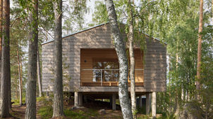 "Located on a small, rocky island in Finland's Lake Suontee, Summerhouse V by Playa Architects is a 71-square-meter retreat completed in 2021. The project was commissioned by a family who found their existing 1960s fishing cabin too small for their needs and wanted a new building better suited for island living. The design draws inspiration from classic summer cabin aesthetics while incorporating modern functionality, with a central goal of connecting the occupants with the serene lake environment.
The architectural response to the island's unique location and occasional strong winds is a practical and aesthetically refined structure. The summerhouse features a protective saddle roof with long eaves, which extends over covered outdoor spaces. These sheltered areas are protected from the wind by external walls that also serve to frame specific views of the lake. The house is intentionally positioned on the flattest and most scenic part of the island, maximizing both the open lake views and access to the evening sun.
Construction was designed for efficiency and minimal environmental impact, using a non-insulated 200 mm thick cross-laminated timber (CLT) frame that could be easily transported and assembled on the island. Computer Numerical Control (CNC) machining of the CLT frame allowed for simple yet elegant detailing. The floor and roof were built with wood fiber insulation and LVL and glulam beams. The spruce frame and interior claddings were mostly left untreated, contributing to a natural, rustic feel. Inside, the main space, which combines the kitchen and living room, is defined by the visible saddle roof and the vast, open view of the lake.
Credits
Architects: Playa Architects
Lead Architects: Tuukka Vuori, Ulla Kuitunen
Photographer: Tuomas Uusheimo
Location: Hirvensalmi, Finland"