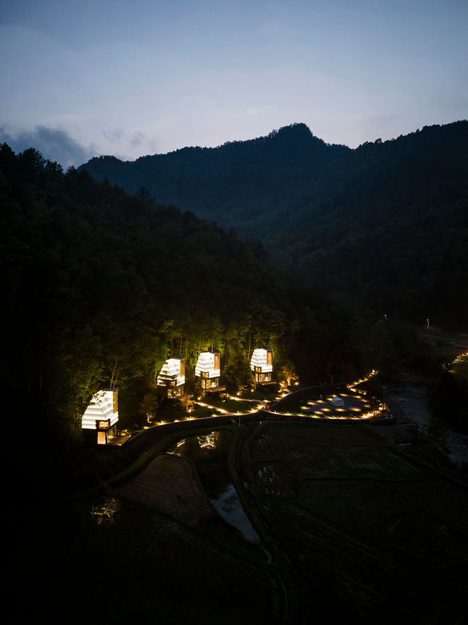 Constructed in 2024 by EERI Studio (Everyday Essentials Research Institute), the Spark Lodges are a set of modular, prefabricated holiday cabins located at the YDD Resort in Changsha, China. The three-story lodges, with a floor area of 76 square meters, were designed for a tourist village in Jinkeng, Hunan, and draw inspiration from the area's rich history, particularly its connection to the fireworks industry. The design harmoniously blends contemporary industrial materials with the natural, rural surroundings of rice fields and the distant Lianyun Mountains.
The exterior of the cabins is composed of green-painted steel frames, pine planks, and most notably, translucent polycarbonate panels that wrap around the roof and certain wall sections. The polycarbonate material, in particular, was chosen for its cost-effectiveness and ability to create a dynamic and "sparkling" effect as light conditions change. These translucent forms give the structures a striking, ethereal quality, especially when viewed against the backdrop of the rice fields and mountains.
The interior of each lodge is designed to create a continuous and changing viewing experience for its occupants. On the ground floor, large, three-sided, floor-to-ceiling windows provide a panoramic, horizontal view of the rice fields, intentionally blurring the line between inside and out. Moving up to the second-floor bedroom, the windows become smaller and more strategically placed, framing "close-up, square-shaped paintings" of the landscape and ensuring privacy. The highest level is a loft space that opens up vertically, offering an expansive view of the distant mountains and framing it like a long, vertical Chinese Shan-shui painting.
Credits
Architects: EERI (Everyday Essentials Research Institute)
Lead Architects: Hou Rui, Zhu Lijin
Location: Changsha, Hunan, China
Year: 2024
Area: 76 m²
Photographs: EERI, NANTU