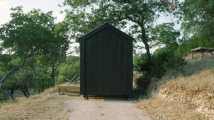 "Elsewhere Cabin A is a 160-square-foot, off-grid prototype designed in 2018 by Seattle-based architect Sean O’Neill for Elsewhere, a vacation rental company near Georgetown, Texas. The tiny cabin was built on a trailer base to allow for off-grid functionality and occasional relocation. Its design was inspired by the traditional Texas porch, aiming to create a serene space for guests to disconnect from city life. This is achieved with a ten-foot folding glass wall that opens the entire living space, creating a large, open-air porch. The exterior is clad in charred cedar siding, a technique known as shou sugi ban, giving it a minimalist black finish that helps it blend into the natural surroundings. The
interior features Chilean pine plywood for the walls, ceiling, and flooring, complemented by custom-made, space-efficient, and multi-functional furniture. A single surface can transition from a desk to a sofa to a kitchen counter. The sleeping loft is nestled beneath the pitched roof, while a small kitchen and a bathroom with a waterless toilet are also incorporated. For off-grid utilities, the cabin relies on solar panels for electricity and an onboard water tank for the shower and sink. Much of the exterior work and some furnishings were built by the client.
Credits
Architects: Sean O'Neill
Photographs: Sean O'Neill
Client: Elsewhere"