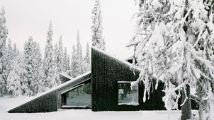 "Designed by Oslo-based Vardehaugen Architects and led by Håkon Matre Aasarød, Cabin Vindheim is a 55-square-meter retreat in the alpine landscape near Lillehammer, Norway, and was completed in 2016 for a private client. The cabin draws inspiration from the classic image of snowbound cabins, where only the roof protrudes through the snow, and blends into its surroundings with deep gables that extend to the ground. The structure's angular shape and black-stained pinewood cladding contrast with the dramatic white winter landscape.
The interior, which is spacious despite its compact size, is clad in a waxed poplar veneer, with uplifts in the sloped ceiling creating a rich spatial experience. An uninterrupted ceiling connects the living room, bedroom, ski room, and a small utility annex. A large, 4-meter-long window in the bedroom offers views of the treetops and night sky, enhancing the feeling of sleeping within nature. The off-grid cabin relies on solar power and a wood oven for energy. A unique and playful feature is the cabin's roof, which doubles as a ski slope or toboggan run during the snowy winters.
Credits
Architects: Håkon Matre Aasarød, Berta Gaztelu, Joana Branco, and Kurt Breitenstein of Vardehaugen Architects
Photography: Rasmus Norlander, Einar Elton"