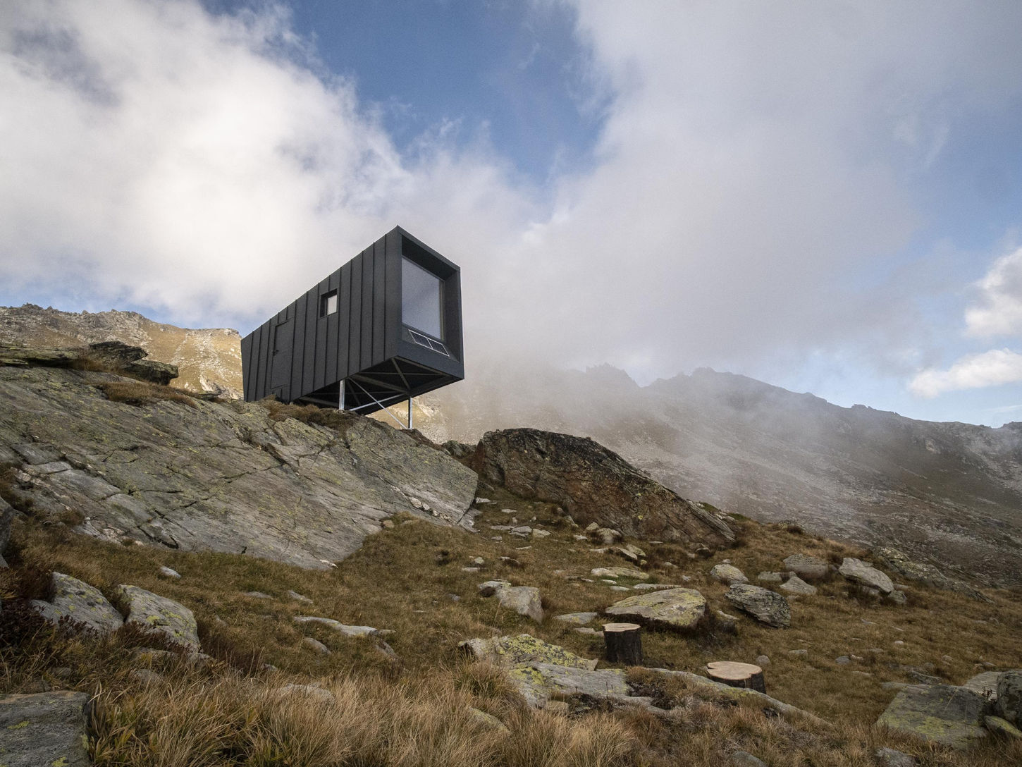 The Bivacco Brédy is a high-altitude mountain shelter designed as a tribute to Claudio Brédy, a local politician and alpinist from Italy's Aosta Valley who tragically died in 2017. Designed by BCW Collective and inaugurated in 2021, the bivouac is set at an altitude of 2,528 meters in the secluded Vertosan Valley, near the alpine lakes of Dzioule. Its design is both functional and deeply symbolic, reflecting Brédy's spirit and connection to the mountains he loved.
The project was initiated by the Brédy family and was the result of an invited competition organized by YACademy and Cantieri d’Alta Quota. The winning proposal by BCW Collective was chosen for its ability to poetically and practically interpret the rugged mountain landscape and honor Brédy's memory.
The cantilevered structure, which appears to launch into the void, is a poignant architectural gesture that evokes the loss of a cherished member of the community. Positioned on a rock slab, the shelter serves as a new landmark in the Vertosan Valley.
The bivouac is designed for both introspection and an immersive experience of the surrounding mountains.
The south-facing shelter is strategically oriented to frame dramatic views of peaks like the Grivola and Gran Paradiso, a summit Brédy had climbed. The minimalist interior focuses occupants on the landscape outside.
The 12 m² interior is functional and warm, clad in wood panels. Six bunks made from climbing cord line the sides, leading to a common area with a large window. A vestibule provides space for gear storage.
The cabin features a solar panel to charge mobile devices, allowing for an off-grid experience.
The bivouac was prefabricated in modules to minimize its environmental impact and facilitate transport to the remote location. The structure was built in three parts, which were then delivered by helicopter and assembled on-site in a matter of days.
A steel frame foundation secures the structure directly to the rock, ensuring minimal disruption to the landscape. This frame supports insulated timber panels. The exterior is covered in dark, aluminum cladding selected for its durability and resistance to harsh weather conditions.
Project credits
Architects: BCW Collective (Chiara Tessarollo, Skye Sturm, and Facundo Arboit)
Construction: Chenevier S.p.a
Photographer: BCW Collective