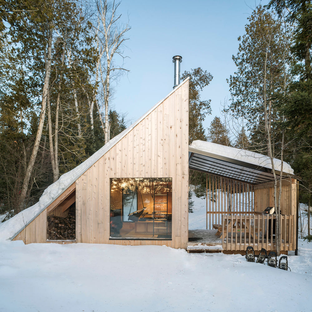 La Pointe is a ready-to-camp micro-shelter designed by the Montreal-based architecture firm Atelier l'Abri for the Poisson Blanc Regional Park, located north of Ottawa in Quebec, Canada. This off-grid, A-frame-inspired cabin offers a unique and minimalist nature immersion for two to four guests. The project was completed in 2019.
The design reinterprets the classic A-frame cabin, popular in North America since the 1950s, with a modern, minimalist aesthetic. The iconic triangular shape creates a simple, sculptural structure while offering a functional and nature-oriented space. The off-grid shelter was built on-site by Atelier l'Abri's construction team, demonstrating a commitment to hands-on, site-specific design. The structure is clad in natural cedar board and batten, which will weather over time to a silvery hue, helping it blend into the forest. A covered terrace expands the living space, creating an ideal spot to enjoy the outdoors even when the weather is less favorable. The long roof is clad in steel, a nod to timeless, rural buildings.
The minimalist and efficient interior makes clever use of space and maximizes natural light. Large bay windows offer uninterrupted views of the forest and the reservoir below, flooding the interior with light. An inclined ladder leads to a lofted bed area, which is suspended from the cathedral ceiling by steel rods, creating a focal point in the space.
The ground floor includes a kitchenette and a dining table that can be converted into an additional bed, accommodating up to four people. A wood-burning stove provides warmth during the frosty Canadian winters, enhancing the cozy cabin atmosphere.
Project credits
Architect: Atelier l'Abri
Construction: Atelier l'Abri construction team
Location: Poisson Blanc Regional Park, Quebec, Canada
Photography: Raphaël Thibodeau
Completion Year: 2019