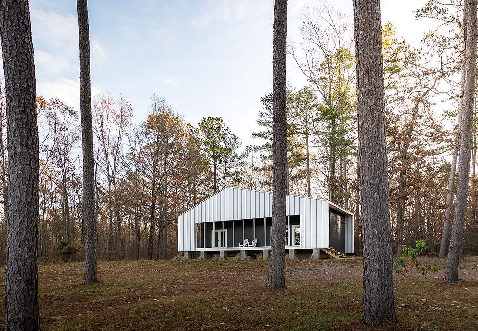 Designed by Memphis-based firm Archimania, the Nash Tiny House is a minimalist weekend home situated on a family property outside of Starkville, Mississippi. Located on the exact site of a fishing trailer that belonged to the clients' father, the tiny house honors the family's history while providing a modern, low-maintenance escape. The property is nestled within a natural clearing of pine, oak, and hickory trees, offering picturesque western views of a pond. 

The tiny house is wrapped in a continuous roof and wall plane, which is clad in durable, low-maintenance metal panels. Galvanized standing-seam panels on the main surface provide a distinct vertical rhythm, while charcoal corrugated metal panels on other walls offer a different texture and scale. The use of concrete masonry units and pressure-treated wood further enhances the home's longevity and minimal upkeep.
 A prominent, full-length front porch extends the living space outdoors and spans the width of the house. It sits within the space created by the continuous roof and wall plane, offering a sheltered spot to enjoy the pond views and natural surroundings.


Interior: In contrast to the metallic exterior, the interior is finished with a warm and simple palette. White-painted pine shiplap siding creates a classic, cozy cabin feel. The floors are polished concrete, adding to the durable, resilient nature of the home.
The efficient 648-square-foot floor plan includes a main living area with an open-plan kitchen. Above the kitchen is a mezzanine sleeping loft, which provides additional sleeping space for guests.
The owner, Jon Nash, a veterinarian who enjoys hands-on work, constructed a significant portion of the home himself, including the kitchen ladder that provides access to the sleeping loft. 

 

Credits 

Architects: Will Randolph of Archimania. 

Clients: Jon and Niki Nash. 

Photography: Archimania  