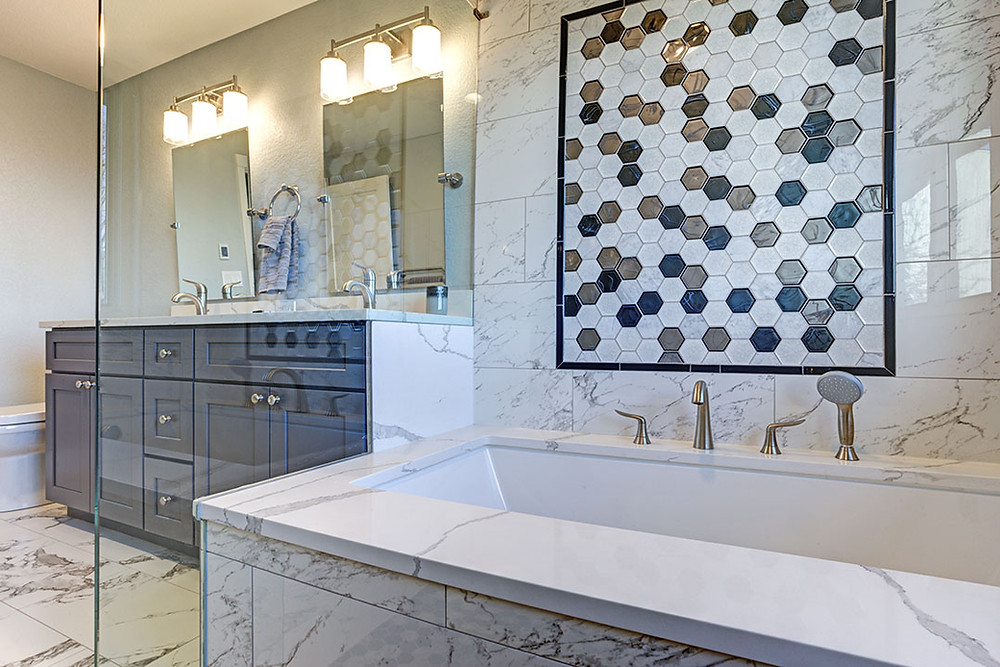 Photo of glass enclosed tub with heavily veined marble surround and octagon black, , white, brown and white inset mural. Grey vanity in background with rectangular mirrors and mounted drop lights.