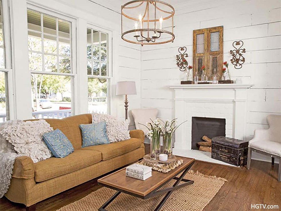 Photo of living room with dark tan sofa, wood floors, tan scatter rug under wood and metal coffee table, brass 3 light chandelier, windows, fireplace, and shiplap wall.