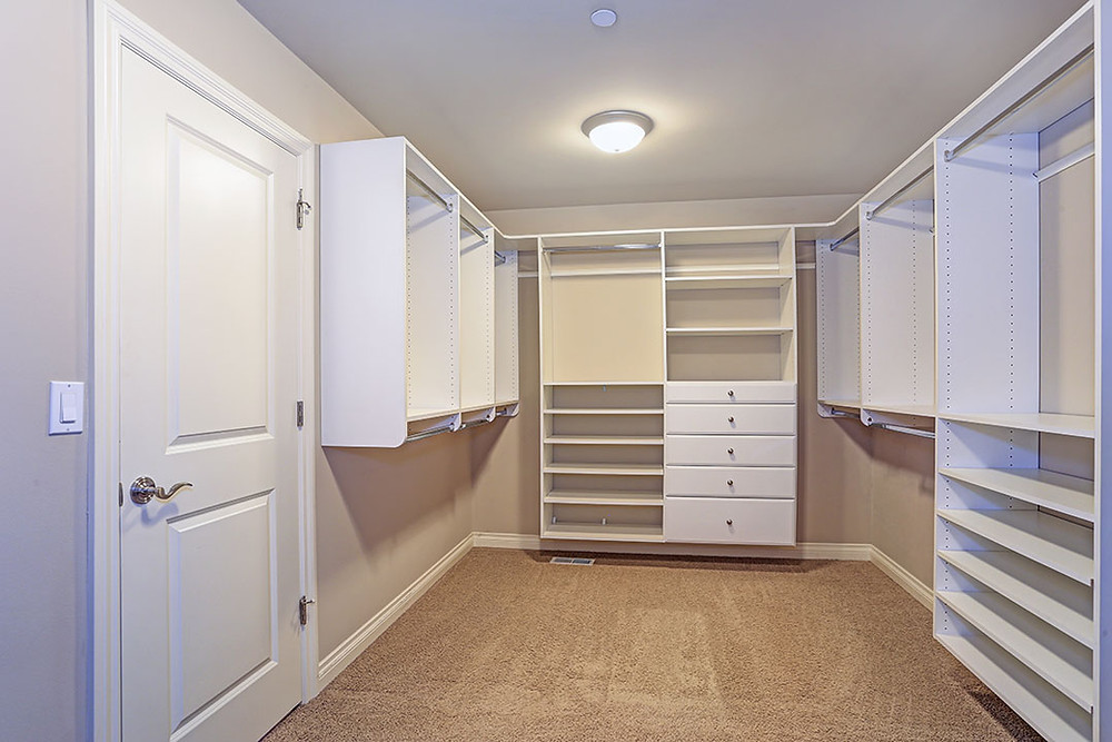 Photo of bedroom converted into walk-in closet with white cabinetry, tan carpeted floor and one ceiling light. No clothes in yet.