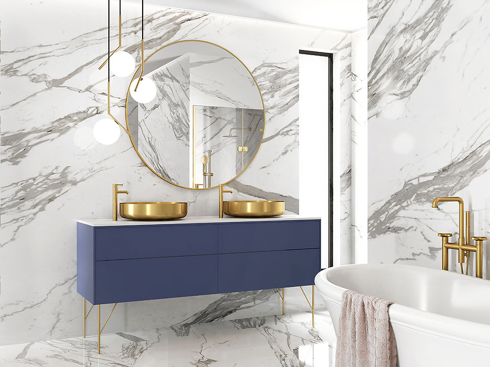 Modern navy suspended bathroom vanity with gold vessel sinks, round gold trim mirror and hanging orb light fixtures, all on heavily veined marble walls and floor.