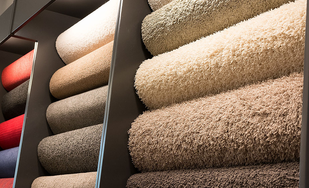 Photo of rolls of carpet on vertical display rack, mostly tans and browns.