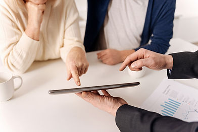 Man holding electronic tablet at table while man and woman clients look and point at it.