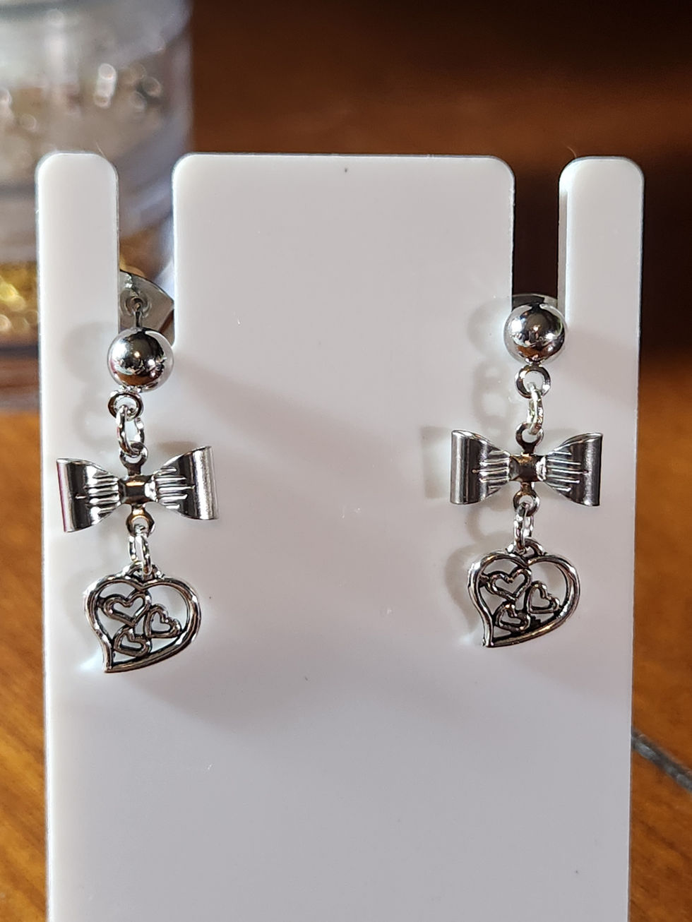Silver stud earrings with bow and heart peace sign charms on display.