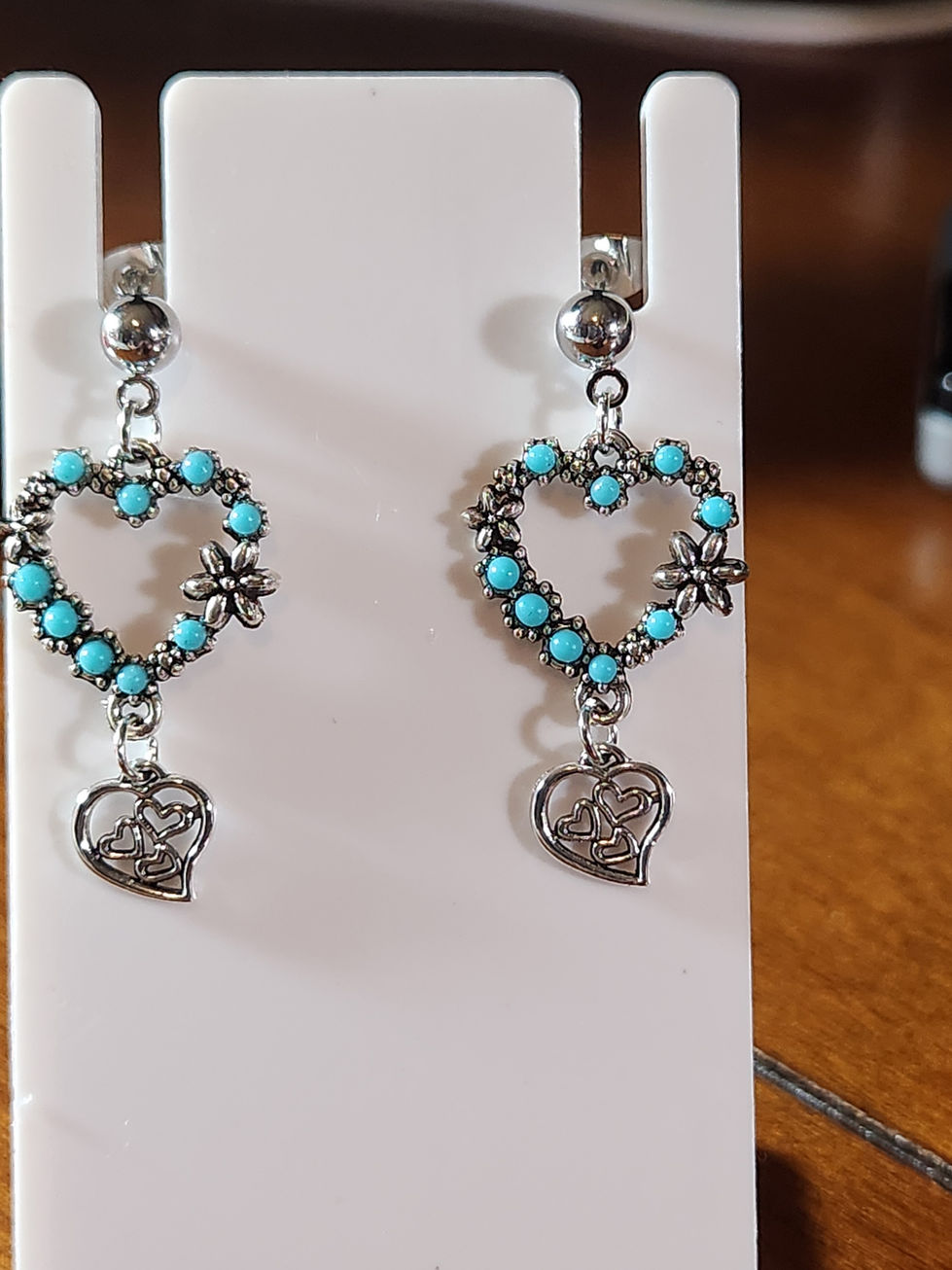 Pair of silver heart earrings with turquoise beads on a white display.