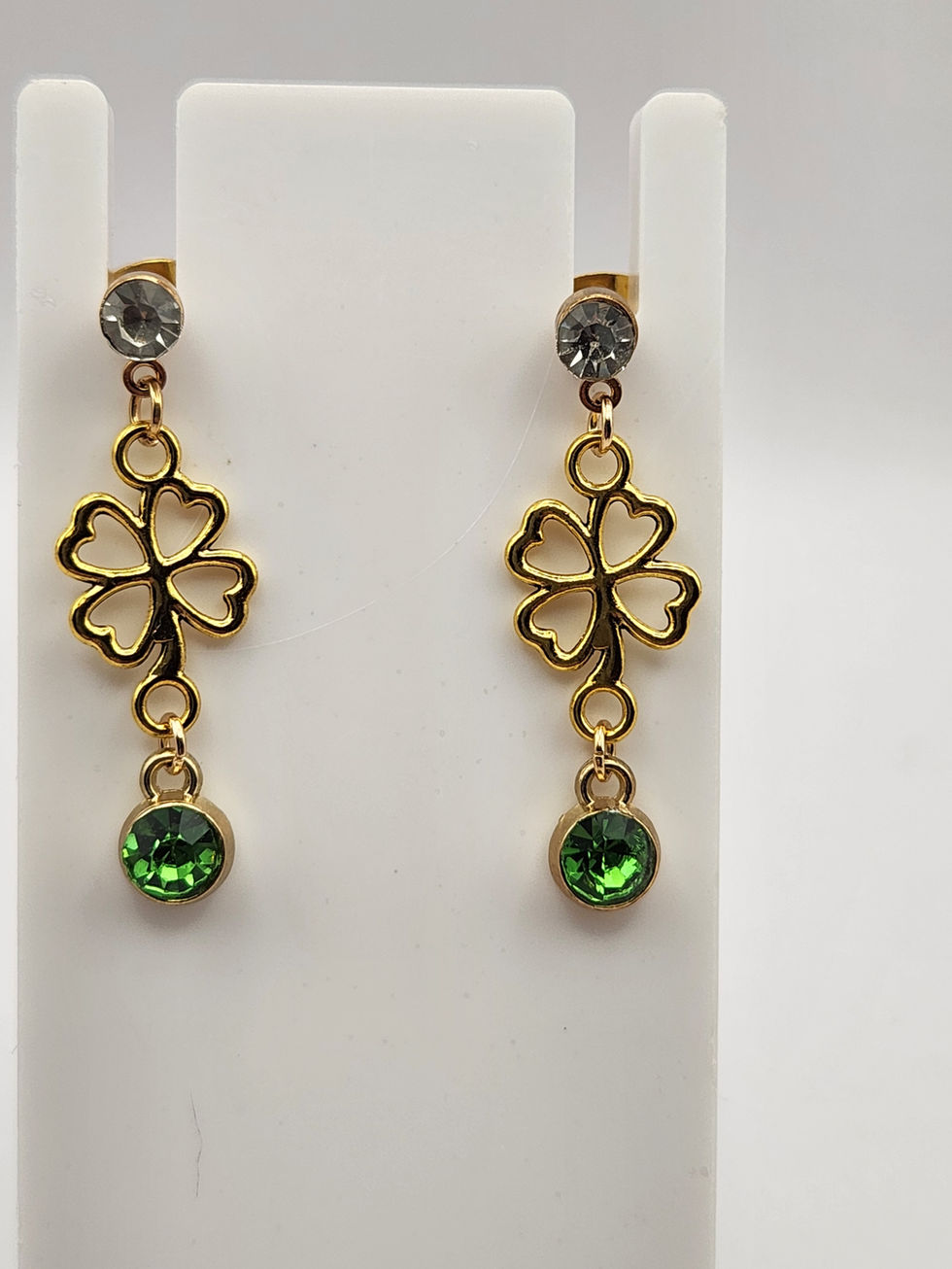 Pair of gold shamrock dangle earrings with clear studs, green gemstones.