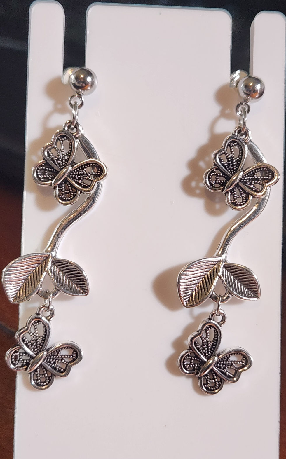 Silver earrings with butterfly and leaf designs displayed on a white stand
