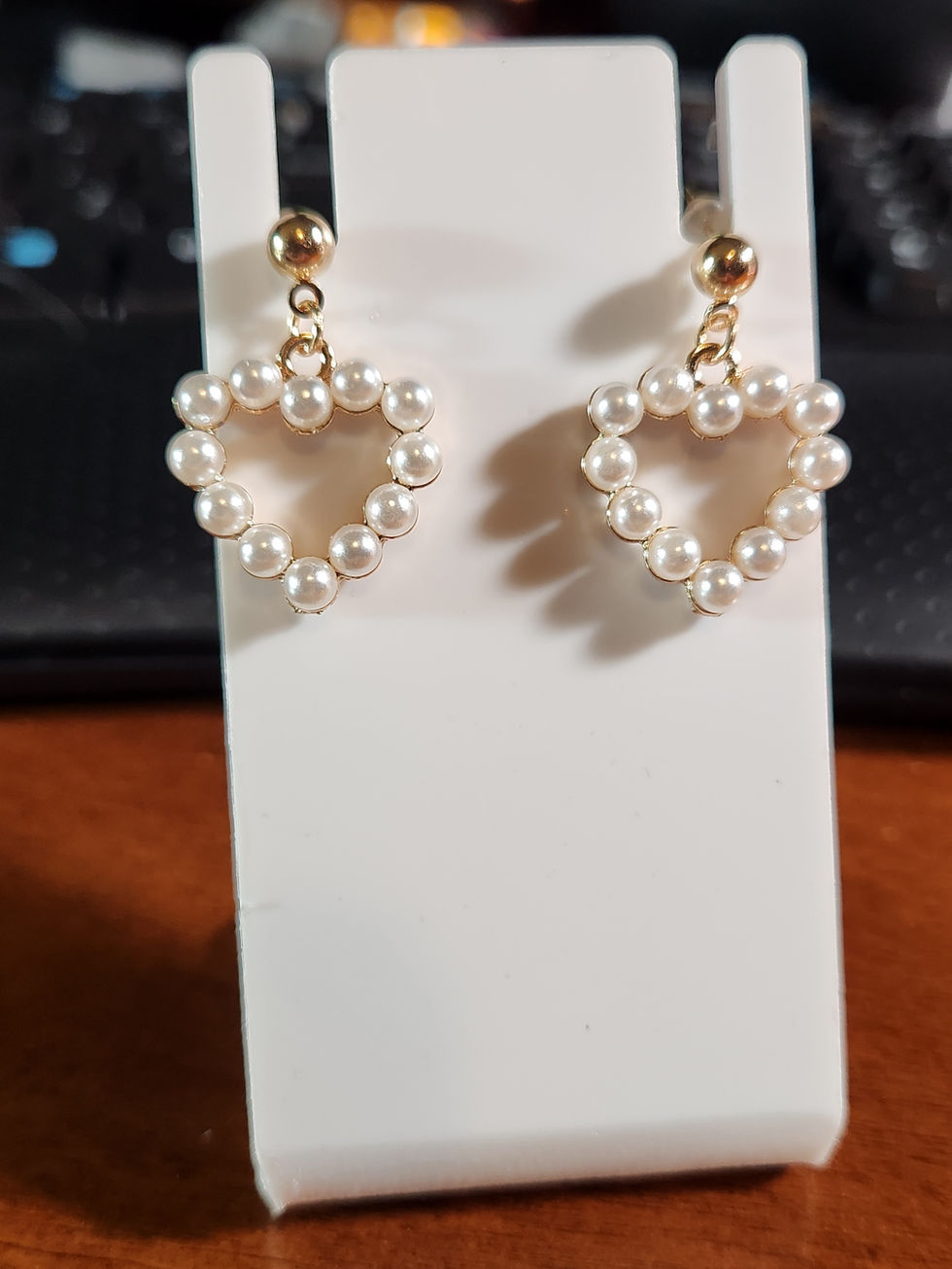 Heart-shaped pearl earrings displayed on a white stand, close-up shot.