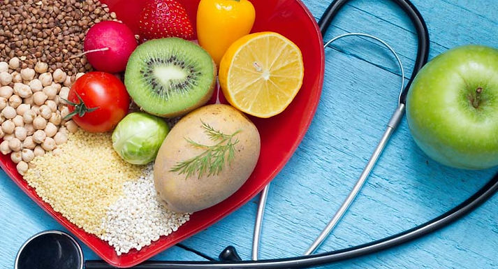l'immagine rappresenta alimenti caratteristici di una dieta sana come kiwi, arance, legumi e ravanelli, all'interno di un piatto da tavola rosso a forma di cuore. Accanto, poggiato su un tavolo azzurro vi è uno stetoscopio, a indicare la stretta relazione tra questi cibi e la salute del cuore.