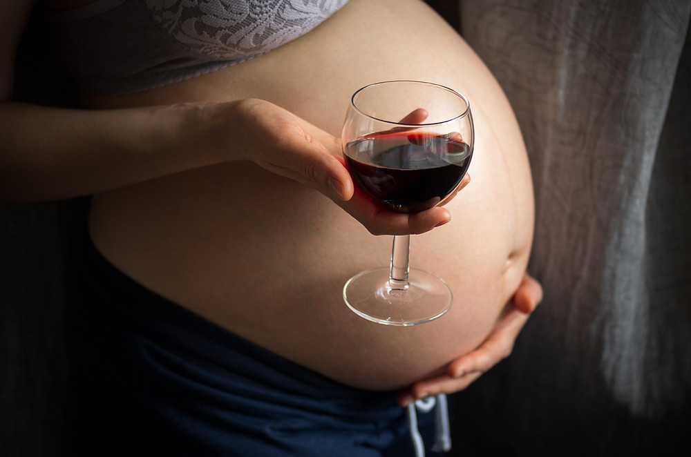 schwangere Frau hält ein Weinglaus in der Hand vor ihrem Babybauch