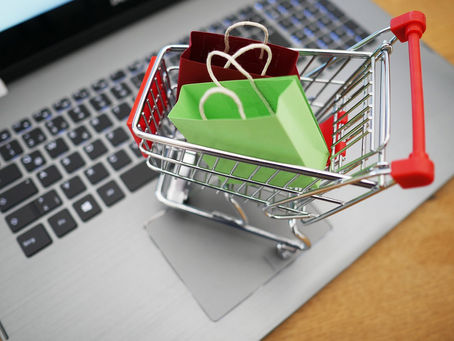 A miniature shopping cart filled with small colorful paper bags rests on a laptop keyboard, symbolizing online shopping and e-commerce.