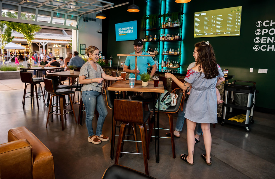 A woman, man, and mother with child playing a table game, enjoying pints of craft beer at The Village Well, a popular destination for family-friendly fun and self-pour craft beverages.